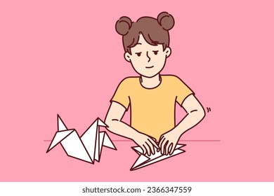 Little girl makes origami bird by folding paper animals and developing own creativity. Child is engaged in origami art, preparing fake for school exhibition and dreaming of becoming sculptor