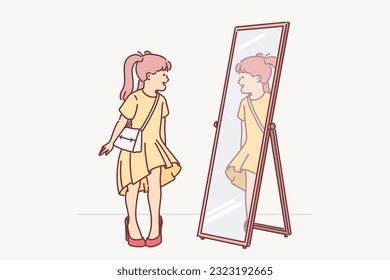 Little girl in mother clothes looks in mirror trying on big shoes with heel and trying to seem like adult. Funny girl for concept of parental happiness or positive emotions from having daughter or son