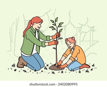 Little girl and mother plant tree in park, helping to restore nature that has suffered from harmful actions of humans. Woman and child plant tree in forest, compacting soil near sprout