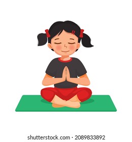 Little girl practicing yoga meditation sitting in lotus pose on a green mat indoor