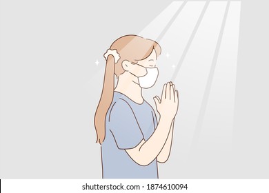  Little girl praying at home during pandemic concept. Little girl in protective medical mask from coronavirus infection staying and playing god with eyes closed hoping to stop infection worldwide 