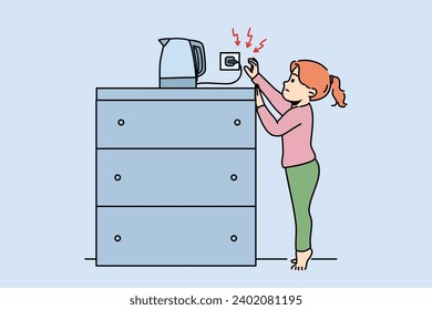 Little girl reaches for socket of electric kettle, risking being burned by hot water or getting electric shock. Child violates safety regulations by touching live electrical appliances.