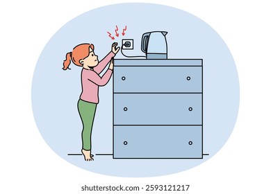 Little girl reaches for socket of electric kettle, risking being burned by hot water or getting electric shock. Child violates safety regulations by touching live electrical appliances.