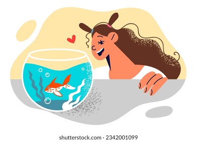 Little girl stands near desktop aquarium with fish and rejoices at appearance of pet given by parents for birthday. Happy child watches inhabitants of aquarium and experiences positive emotions