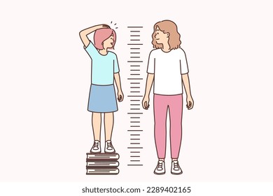 Little girl stands on books measuring growth and wants to compete with older sister. Funny child wishes to get up as soon as possible as adult and cheats competing with girl friend in checking growth 