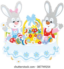 Little grey rabbits decorating a basket of painted Easter eggs with flowers