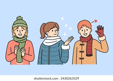 Little kids in winter clothes stand under falling snow, rejoicing at onset of christmas weekend at school. Cheerful boys and girls waving hands and catching snowflakes during christmas holidays