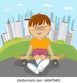 Little nerd boy sitting on a skateboard in park in front of downtown