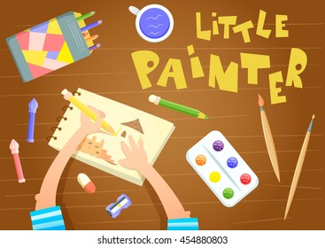Little painter sitting at table and drawing in sketchbook. Art supplies - felt pen, colored pencils, paint box, paintbrush, plastic palette are on wooden table. Child artist. Preschooler homework.