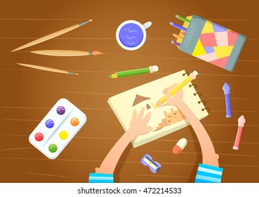 Little painter sitting at table drawing in sketchbook. Art supplies - felt pen, colored pencils, paint box, paintbrush, palette, pencil sharpener on wooden table. Child artist. Preschooler homework.