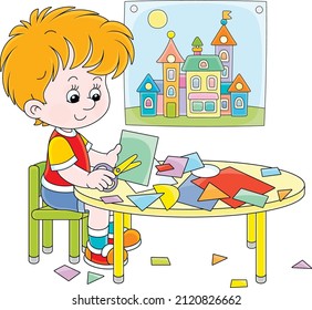 Little preschool child cutting outlines and figures from color paper with scissors and making a funny picture of a pretty toy town, vector cartoon illustration isolated on a white background