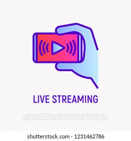 Live streaming thin line icon: hand holding smartphone with play button. Video blogging. Modern vector illustration.