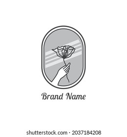 a logo with a hand holding a flower theme with a mirror background behind it, for boutique companies, fashion, etc