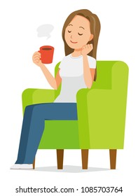 A long hair young woman is sitting on a sofa and drinking coffee