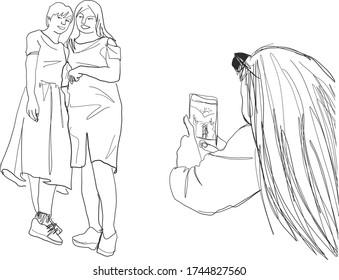 A long haired woman using a smartphone to take pictures of her friends standing and smiling happily.