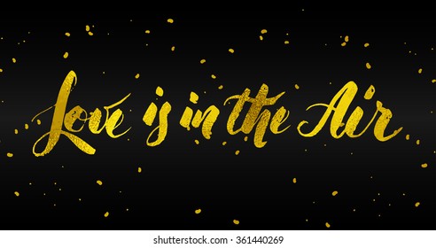Love is in the air quote hand written lettering by brush. Bold glitter texture over text with small golden ink dots over black background.
