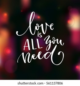 Love is all you need. Romantic saying for Valentine's day card. Modern calligraphy handwritten on blurred background with lights and bokeh