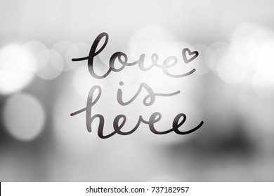 love is here lettering, vector handwritten text on blurred lights