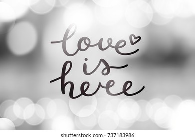 love is here lettering, vector handwritten text on blurred lights