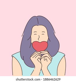Love story or Valentines day concept. Young smiling girl covers her mouth with a paper red heart.