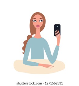 Lovely happy young Beautiful Caucasian girl with brown wavy hair in ponytale wearing blue top sitting at table holding mobile phone in her hand Taking picture Make selfie Modern Technology concept