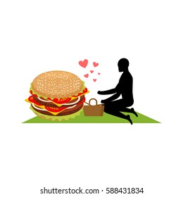lover fast food. Man and hamburger on picnic. Guy and Burger. Meal in nature. blanket and basket for food on lawnt. Romantic date fastfood. Glutton Lifestyle