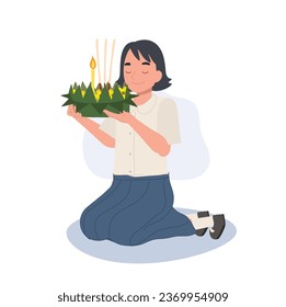 Loy Krathong Traditional Festival. Thai Student girl is sitting and hold krathong up to make a wish before float in river.