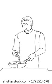 male chef stands over a deep frying pan, in which a large spoon is stirring the dish being prepared, with his other hand he holds the handle