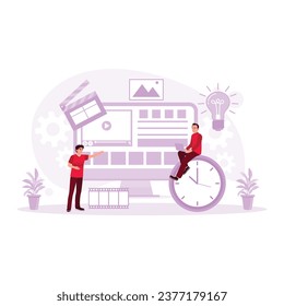  A male editor sits on a wall clock and uses a laptop to edit a video a colleague points to on the computer screen. Video Editor concept. trend modern vector flat illustration
