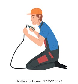 Male Electrician Engineer Sitting on His Knee Repairing Cable with Pliers, Electricity Maintenance Service Worker Character in Uniform and Cap Cartoon Style Vector Illustration