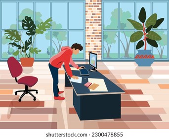 A male employee in the office stands over a table with a laptop and documents. Office landscaping. Bright room for workshop. Freelancer workplace at home.