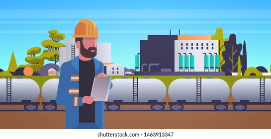 male engineer in helmet using tablet controlling train tanks with oil and fuel factory building industrial zone plant power station production technology concept horizontal