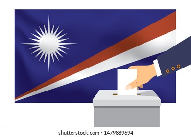 Male hand puts down a white sheet of paper with a mark as a symbol of a ballot paper against the background of the Marshall Islands flag. Marshall Islands the symbol of elections.
