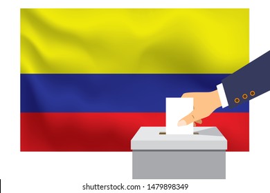 Male hand puts down a white sheet of paper with a mark as a symbol of a ballot paper against the background of the Colombia flag. Colombia the symbol of elections.
