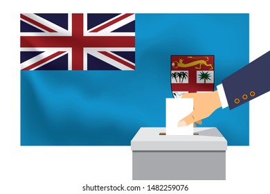 Male hand puts down a white sheet of paper with a mark as a symbol of a ballot paper against the background of the Fiji flag. Fiji the symbol of elections.