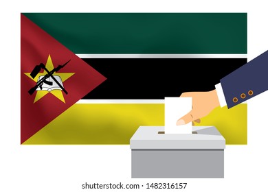 Male hand puts down a white sheet of paper with a mark as a symbol of a ballot paper against the background of the Mozambique flag. Mozambique the symbol of elections.