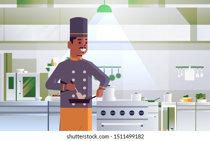male professional chef using frying pan stirring food african american man in uniform standing near stove cooking concept modern restaurant kitchen interior portrait horizontal
