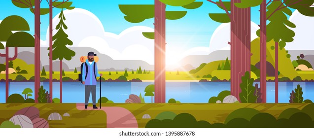 male tourist hiker with backpack african american man traveler holding stick standing in forest hiking concept sunrise landscape nature river mountains background horizontal full length