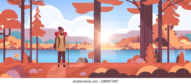 male tourist hiker with backpack man traveler holding stick standing in forest hiking concept sunrise autumn landscape nature river mountains background flat horizontal full length flat