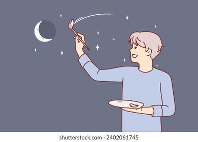 Man artist paints evening sky with moon and stars, dreaming of traveling around galaxy. Young guy artist with brush to create artistic shader and palette smiling doing creative hobby