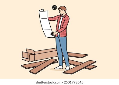 Man assembles furniture with own hands and holds large paper instruction manual, standing among boards. Young guy who assembles furniture is feeling unsure due to lack of experience.