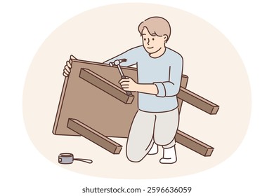 Man assembles table buying it in furniture store and repairs DIY wooden desk for kitchen. Guy is assembling furniture using screwdriver to fix legs during DIY repairs in appartment