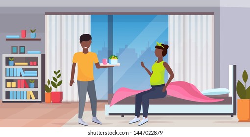 man bringing breakfast tray with food for pregnant woman sitting on bed african american family in love pregnancy concept modern home bedroom interior full length horizontal flat