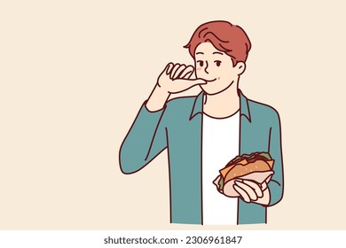 Man with burger licks fingers and enjoys reception of fast food bought in street restaurant or ordered for delivery. Smiling guy holding tasty cheese burger while eating sandwich with cutlet