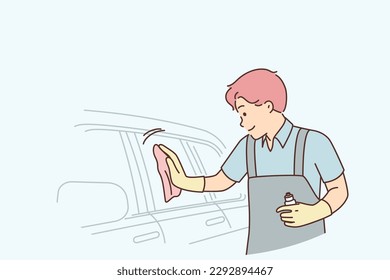 Man car wash employee polishes glass of sedan using special spray to add shine and repel water. Guy works at car wash and provides services for polishing and cleaning customers vehicles. 