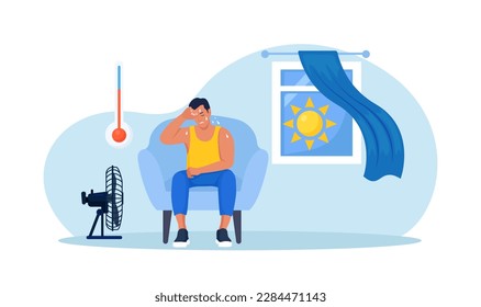 Man chilling on armchair under cooling fan, under blowing air at home. High temperature, hot weather. Summer. Exhausted tired person suffering from heat stroke. Overheating and exhaustion. Dehydration