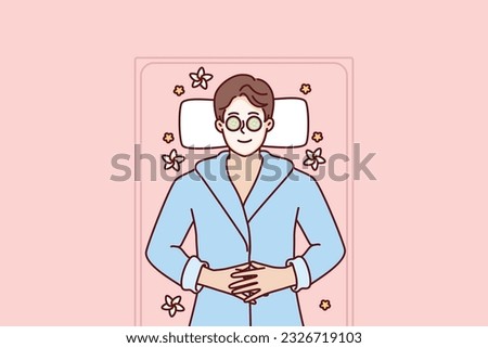 Man with clay mask on face lies in SPA during rejuvenation and anti-wrinkle treatment. Guy with cucumbers on eyes smiles being in SPA salon and restoring strength after hard day work