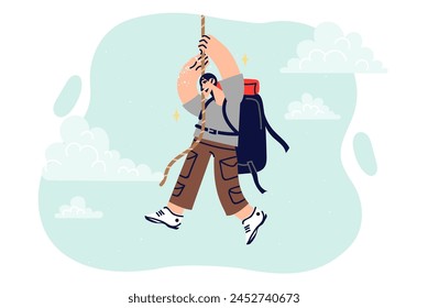 Man climber climbs rope hanging from sky, enjoys extreme sports and outdoor activities. Rock climber guy with tourist backpack on back takes part in hike overcoming difficult obstacles.