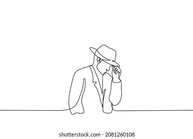 man in coat and wide brimmed hat slightly tilted his head down adjusting his hat - one line drawing vector. concept man in vintage stylish twentieth century men clothing for cold weather