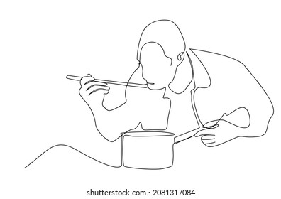 Man cooks in the kitchen and tastes, tests and measures food from the pot with a spoon. A man who cooks his own food at home.